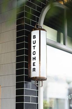 a sign that says butcher hanging on the side of a brick wall next to a window