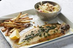 a white plate topped with fish and french fries next to a bowl of coleslaw