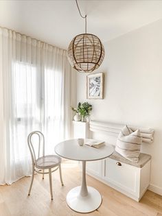 a table and chairs in a room with white walls, wood flooring and curtains