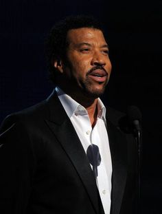 a man in a black suit and white shirt standing next to a microphone with his mouth open