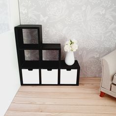 a vase with flowers on top of three cubes in front of a wallpapered room