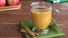 a glass mug filled with liquid sitting on top of a green napkin next to cinnamon sticks