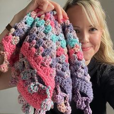 a woman is holding up a crocheted blanket