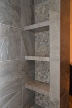 a walk in shower sitting next to a white tiled wall and wooden shelves on the side