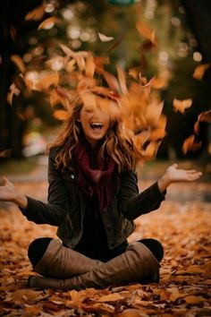 a woman is sitting on the ground with her hands in the air and falling leaves