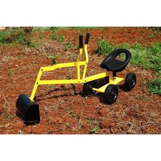 a small yellow cart with two black wheels on the ground in front of some grass