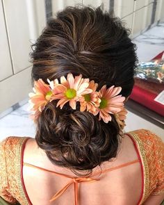 the back of a woman's head with flowers in her hair and an orange top