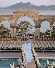 an outdoor ceremony set up with white flowers and greenery in front of the water