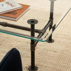 a glass coffee table with metal legs on carpeted floor next to books and magazines