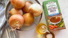 some onions and carrots are on a table next to a carton of organic vegetable broth