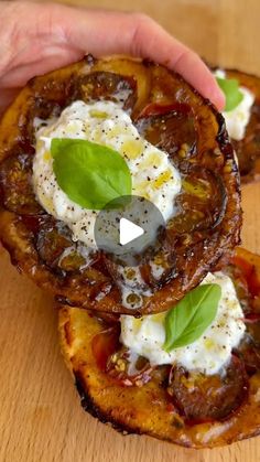 two pieces of bread with cheese and basil on top, being held by someone's hand