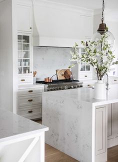 a white kitchen with marble counter tops and an island in front of the stove top