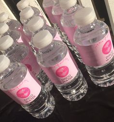 six bottled water bottles are lined up on a black counter top with pink labels and white caps