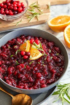 cranberry sauce in a pan with orange slices and rosemary garnish on the side