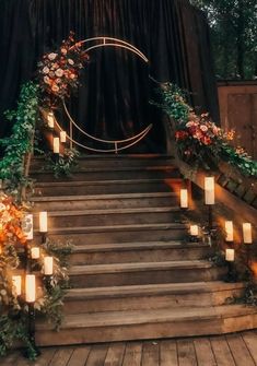 an outdoor ceremony with candles and flowers on the steps leading up to the stage that is decorated with greenery