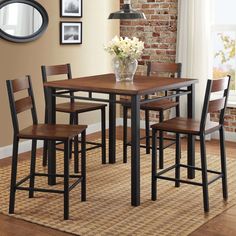 a dining room table with four chairs and a vase on top of it in front of a brick wall