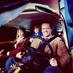 three people are sitting in the back of an old car, one is holding a steering wheel