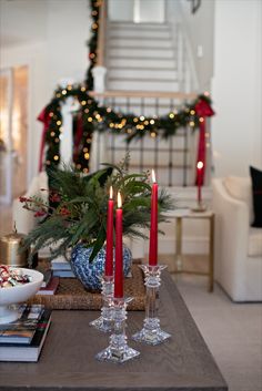 two candles are lit on a table in front of a christmas tree and staircase case