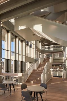 an empty room with tables and chairs in front of large windows, stairs leading up to the second floor