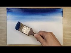 a hand holding a paint brush over a piece of paper with blue and white stripes on it