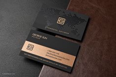 two black and gold business cards sitting on top of a brown leather tablecloth next to each other