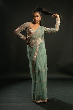 This enchanting dusty turquoise saree is crafted from delicate net fabric, radiating an ethereal charm that captivates the imagination. Paired with a matching net blouse adorned with a flair of pink, it emanates a bridal and festive aura that is simply irresistible. So mesmerizing is its allure that one might be compelled to invent an occasion just to don its elegance and grace. Perfect for weddings, celebrations, or any special event, this saree is a true embodiment of beauty and festivity, des Bollywood Style Turquoise Pre-draped Saree, Turquoise Bollywood Pre-draped Saree, Fitted Turquoise Saree For Diwali, Fitted Turquoise Saree, Turquoise Fitted Saree With Zari Work, Bollywood Style Turquoise Blouse Piece For Wedding, Wedding Turquoise Blouse Piece With Cutdana, Net Pre-draped Saree With Self Design, Festive Pre-draped Saree With Self Design