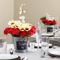 the table is set with silverware and flowers in buckets on top of it