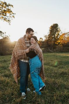 a man and woman wrapped up in a blanket standing on top of a grass covered field