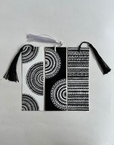 three black and white bookmarks with tassels hanging from the front, on a white background