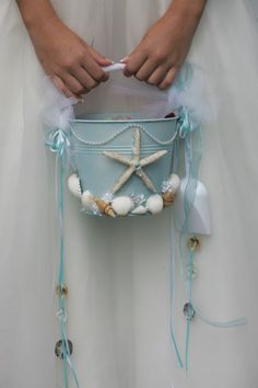 a person in a white dress holding a blue bucket with starfishs and seashells