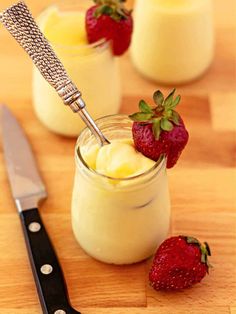 two jars filled with pudding and strawberries next to a knife on a cutting board