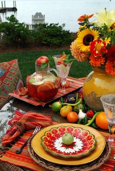 an outdoor table set with plates, glasses and vases filled with flowers on it