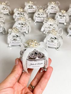 a hand holding a small ring in front of a bunch of tiny rings with pearls on them