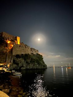 the moon shines brightly over an old castle on top of a cliff overlooking the ocean