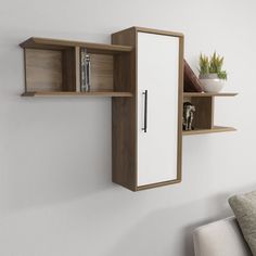 a white and brown wall mounted shelf next to a couch with a plant on it