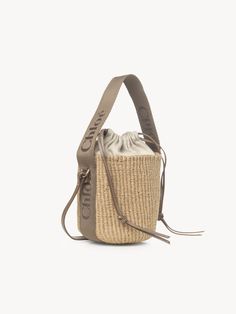 Chloé Small Woody Basket In Fair Trade Natural Fibers | Chloé US Leather Bucket Bag With Braided Handles In Basket Shape, Straw Pouch Bag With Braided Handles For Shopping, Shopping Straw Pouch Bag With Braided Handles, Beige Woven Leather Bucket Bag, Beige Leather Basket Bucket Bag, Braided Handles Straw Pouch Bag For Shopping, Eco-friendly Bucket Bag With Braided Handles, Eco-friendly Bucket Bag With Leather Handles, Eco-friendly Top Handle Bucket Bag With Leather Handles