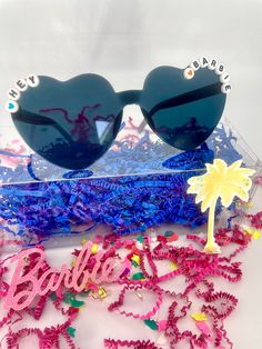 sunglasses and confetti are on display in a clear plastic box with the word barbie written across it