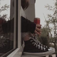 a person holding a drink in their hand while sitting on a window sill outside