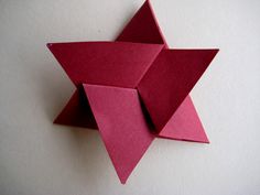 an origami star on a white wall with red paper folded in the shape of a flower