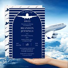 a hand holding up a blue and white graduation card with an airplane in the background