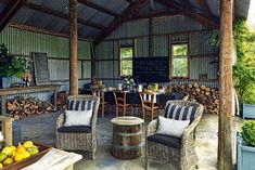 an outdoor dining area with wicker furniture and wood burning firewood in the background