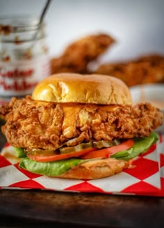 a chicken sandwich with lettuce, tomato and onion on a checkered napkin