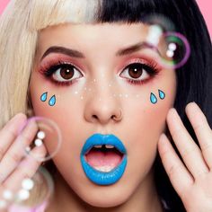 a woman with blue lipstick and rain drops on her face is blowing bubbles in the air