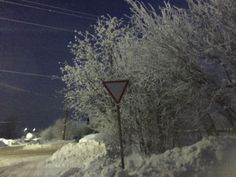 a red triangle sign sitting on the side of a snow covered road next to trees