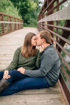 a man and woman sitting on a bridge kissing