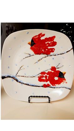 a white plate with two red birds painted on it and snowing around the branches