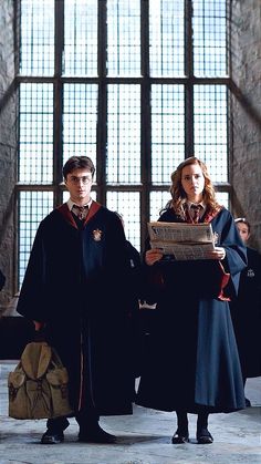 two harry potters standing in front of a window with their robes on and one holding a book