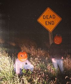 two children sitting in the grass with pumpkins on their heads near a dead end sign