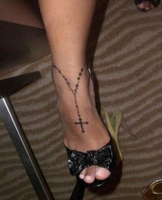 a woman's foot with a cross tattoo on her left leg and a black bow tie around the ankle