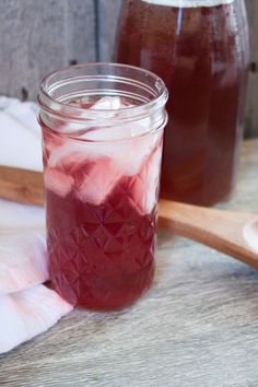 two mason jars filled with liquid sitting on top of a wooden table next to a spoon